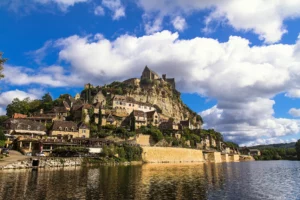 Beynac-et-Cazenac — Le village de Beynac étagé sous son château, se reflétant dans la Dordogne, sous de grands nuages.