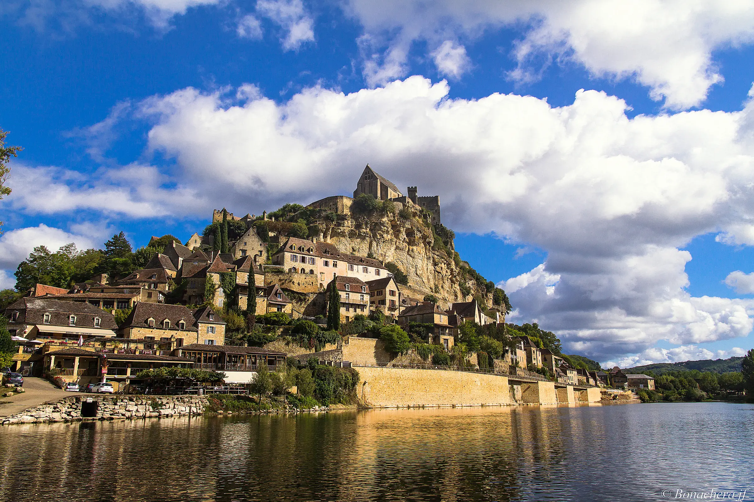 Beynac-et-Cazenac — Le village de Beynac étagé sous son château, se reflétant dans la Dordogne, sous de grands nuages.