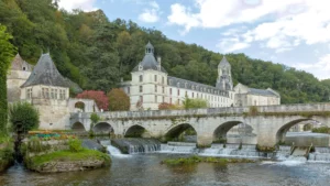 Brantôme — La Dronne, le pont coudé et l'abbaye au pied du coteau boisé.