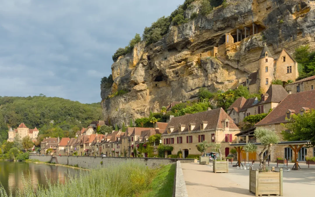 La Roque-Gageac — Les maisons aux toits bruns alignées au pied de la grande falaise, vues depuis la rive.