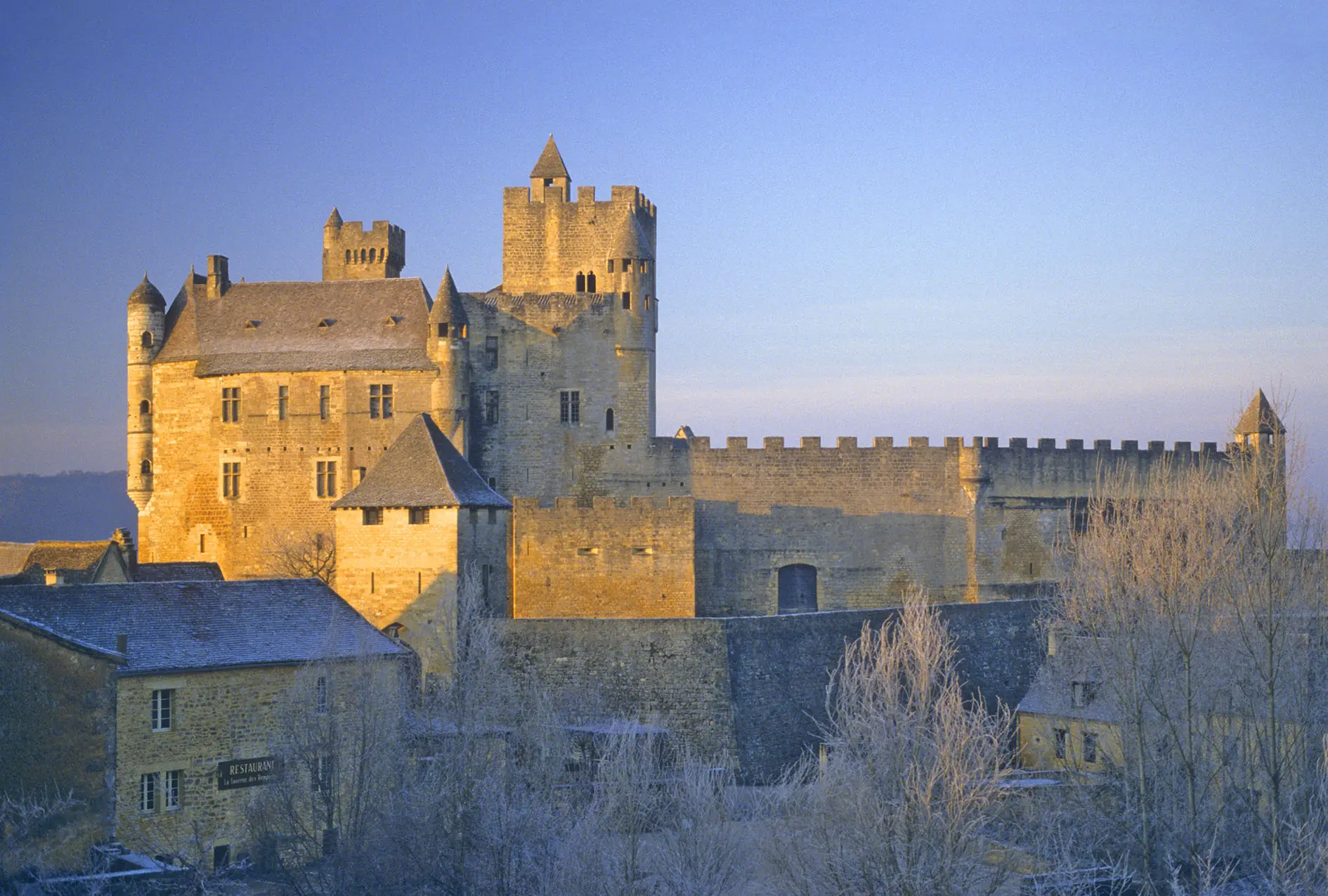 Le château de Beynac doré par le soleil levant, toits et arbres couverts de givre