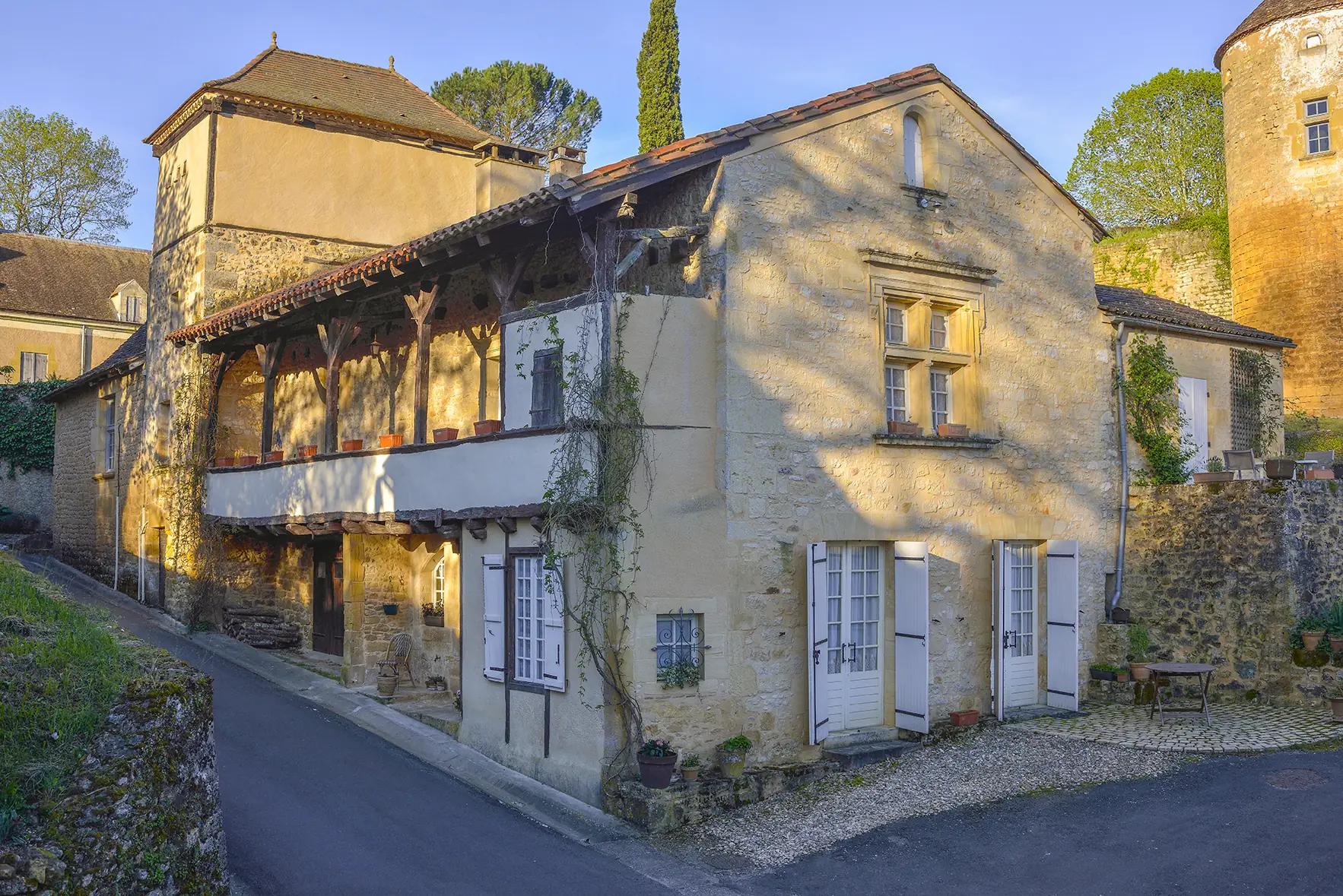 Une maison ancienne à galerie de bois dans une ruelle de Montferrand-du-Périgord, avec une tour du château