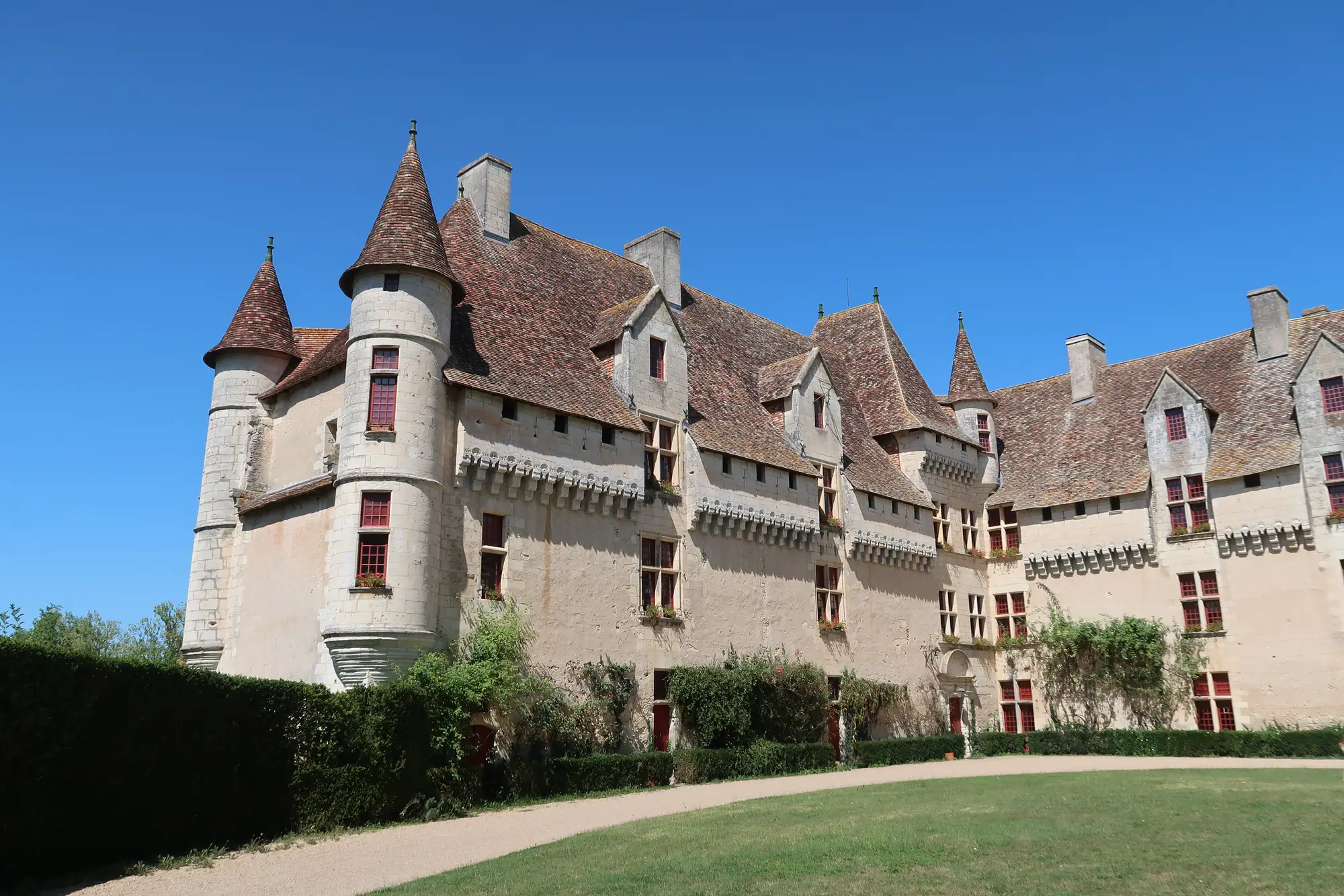 Le château de Neuvic, ses tours coiffées de tuiles et sa longue façade Renaissance, au-dessus d'une pelouse